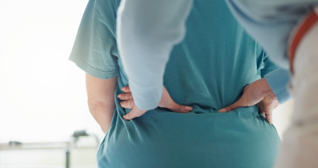Close-up of a healthcare provider examining an older adult's lower back during a clinical evaluation for back pain.