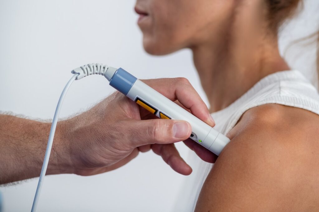 A physical therapist performs laser therapy on a patients shoulder to reduce pain, decrease inflammation, and promote tissue healing, aiding in faster recovery and improved mobility