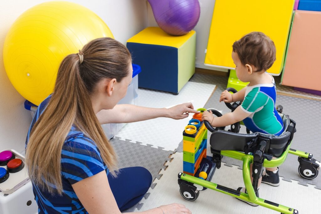 Physiotherapist assists a young boy with musculoskeletal disorders using mobility aids during rehabilitation exercises
