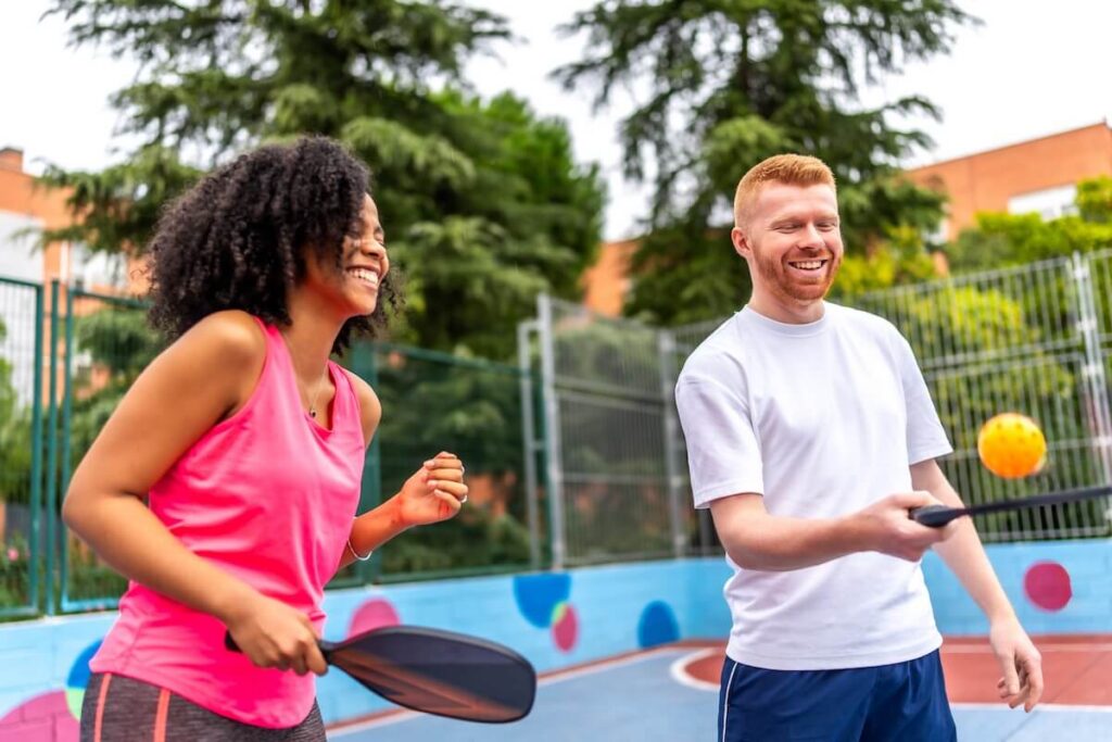 Two players smiling and enjoying a friendly pickleball game in a relaxed outdoor setting.