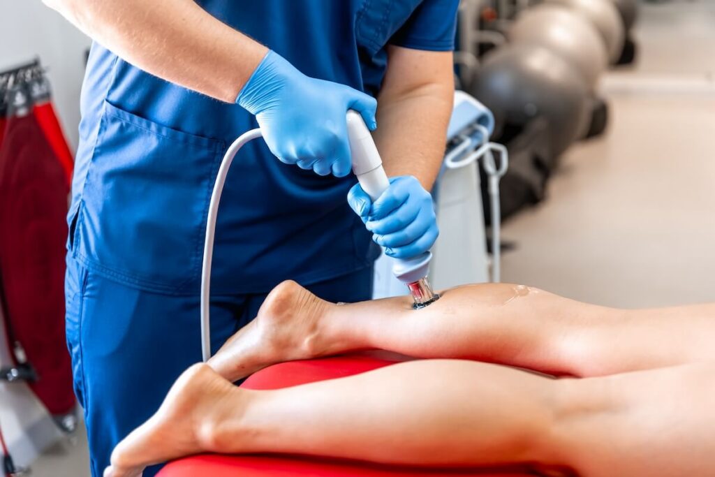 physical therapist using shockwave therapy on patient's shin