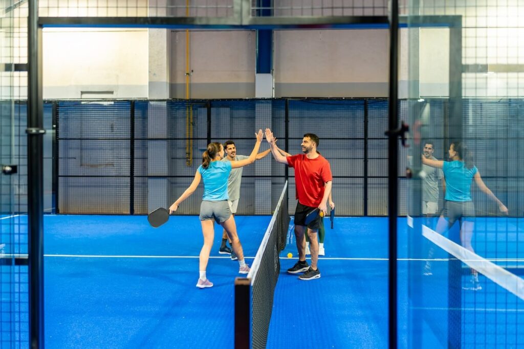 Players high-fiving across the net after a point in an indoor pickleball court.