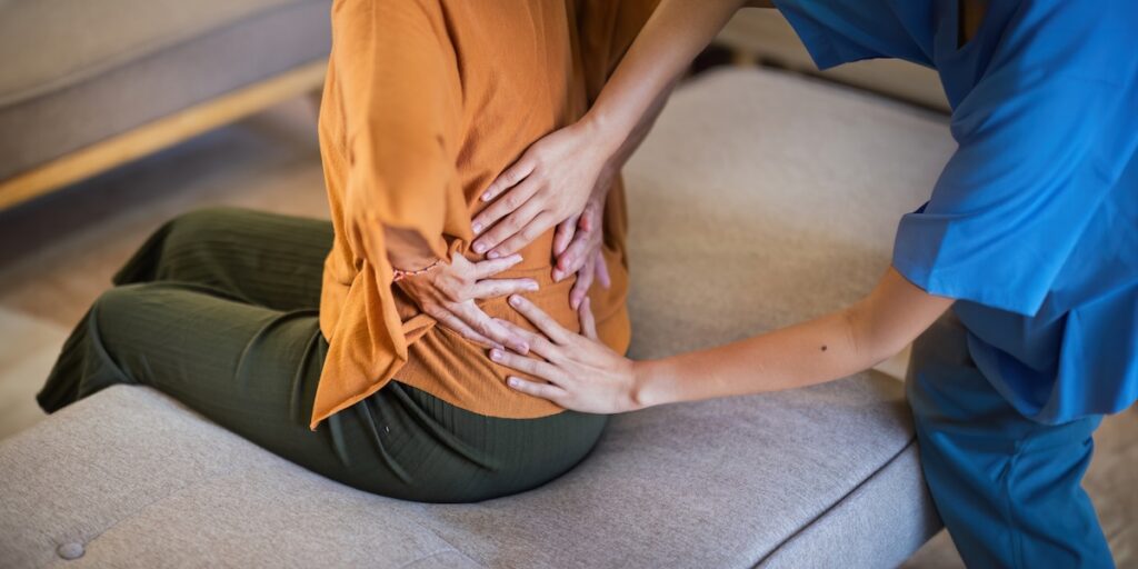 Physical therapist assisting a patient with lower back treatment and posture support.